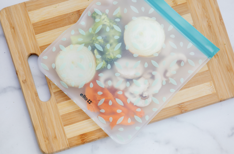 A plastic bag filled with vegetables is sitting on a wooden cutting board.