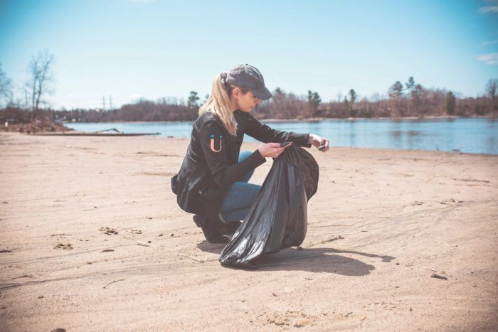 A woman is kneeling on the beach with a trash bag.