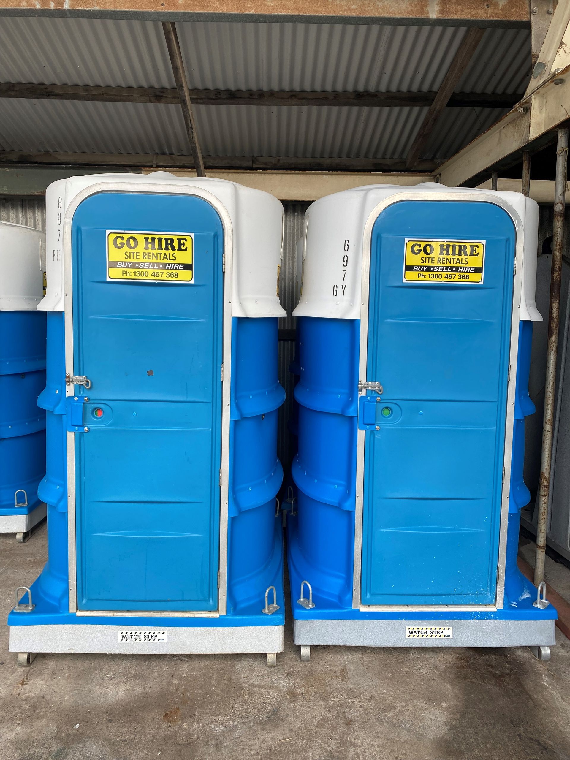 Two blue portable restroom units with white roofs stored inside a metal shed.