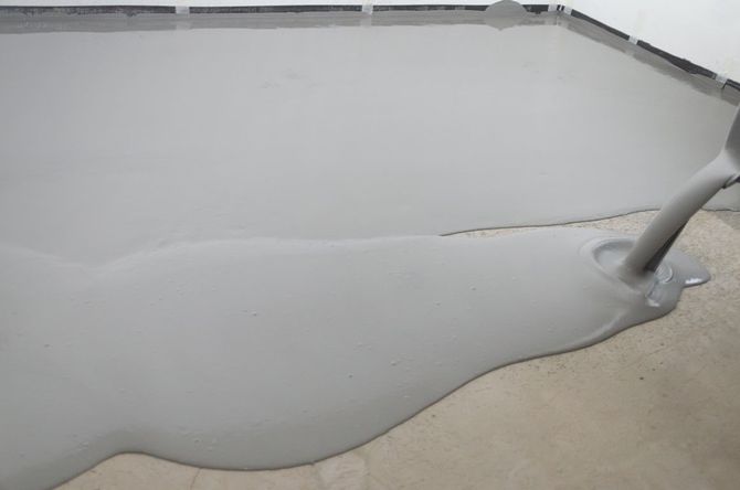 Gray liquid spread on a concrete floor, with a tool or hose at the right edge.