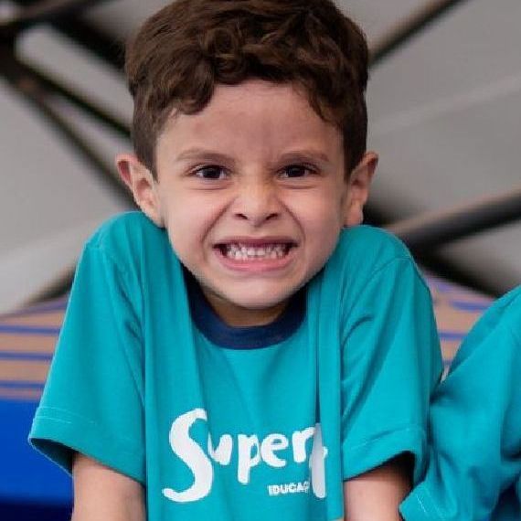 um menino vestindo uma camisa azul com a palavra super+ está sorrindo.
