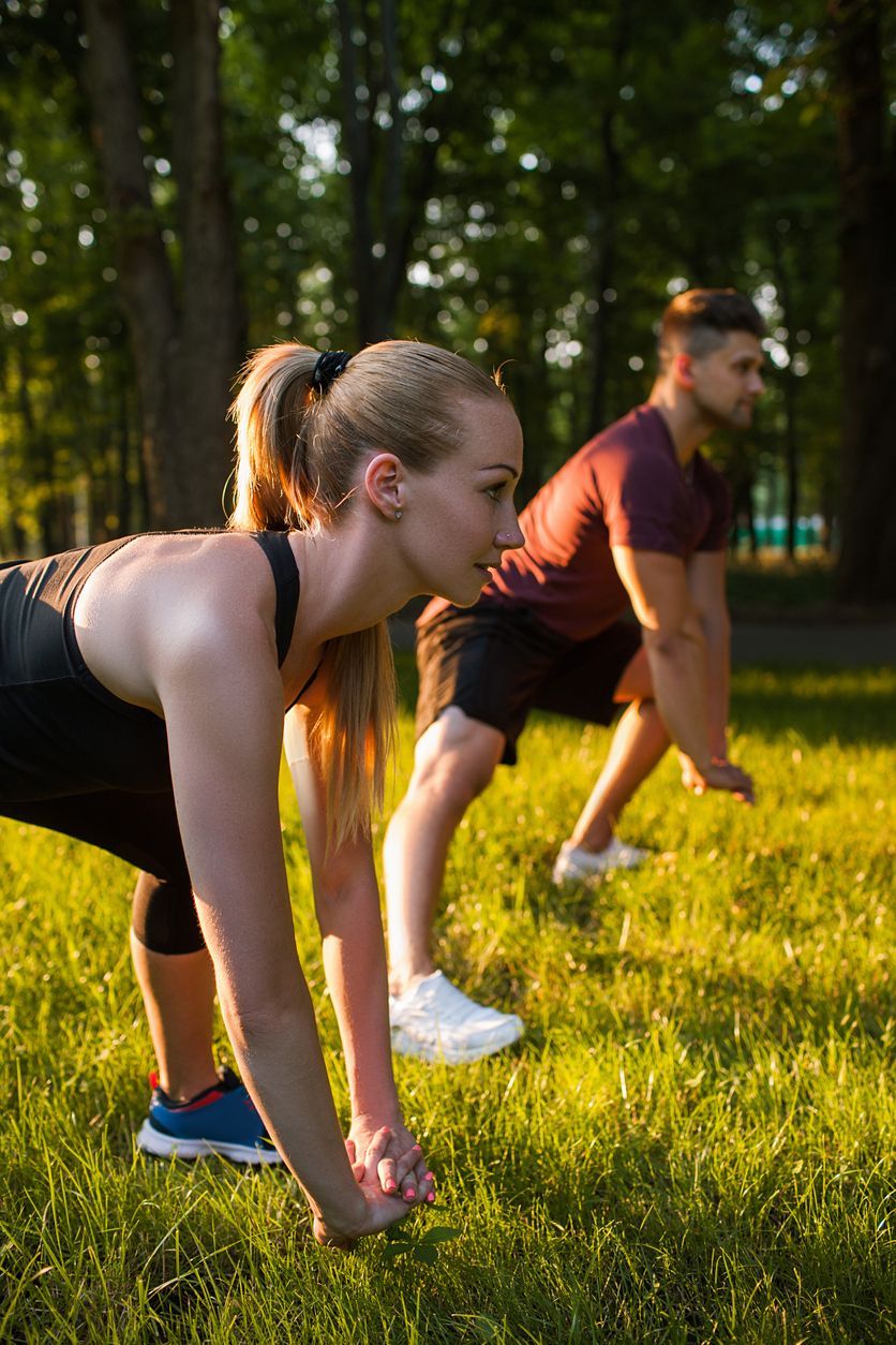 Un hombre y una mujer están haciendo flexiones en el césped de un parque.