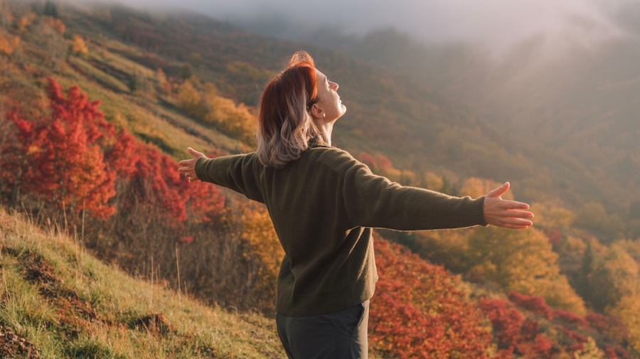 Woman with arms outstretched enjoying a scenic mountain view with colorful fall foliage.