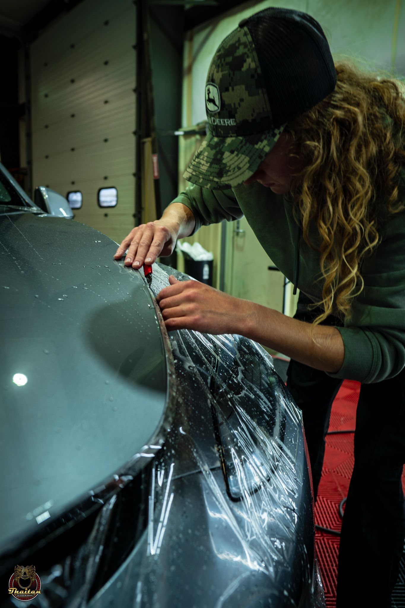 A woman is wrapping the hood of a car in plastic.