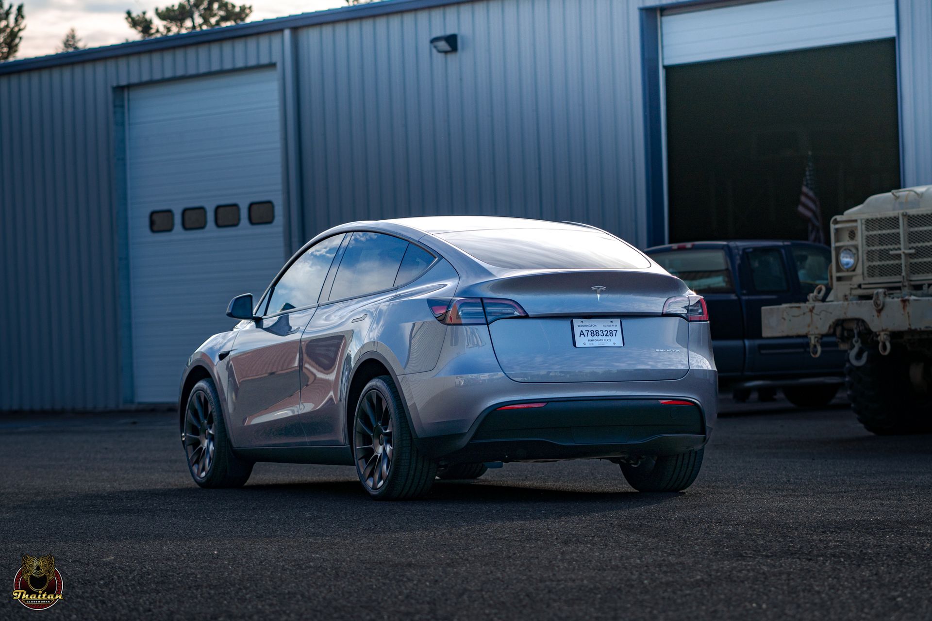 A silver tesla model y is parked in front of a garage.