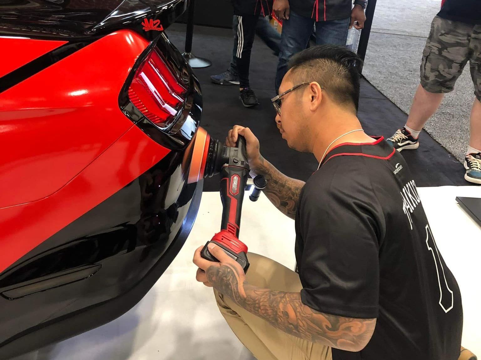 A man is polishing a red car with a polisher.