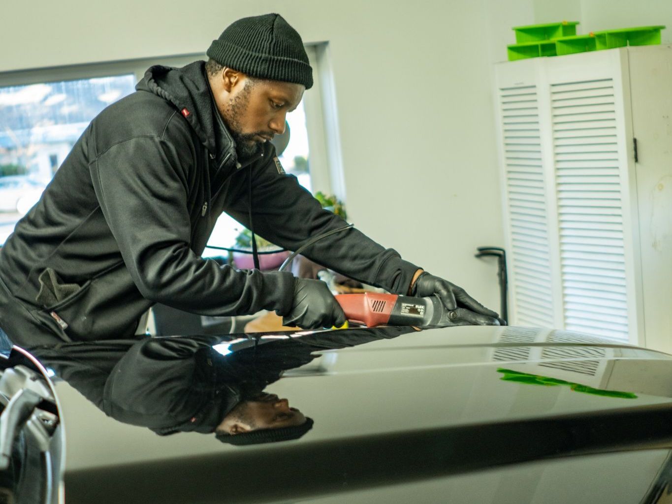 A man is polishing the hood of a car in a garage.