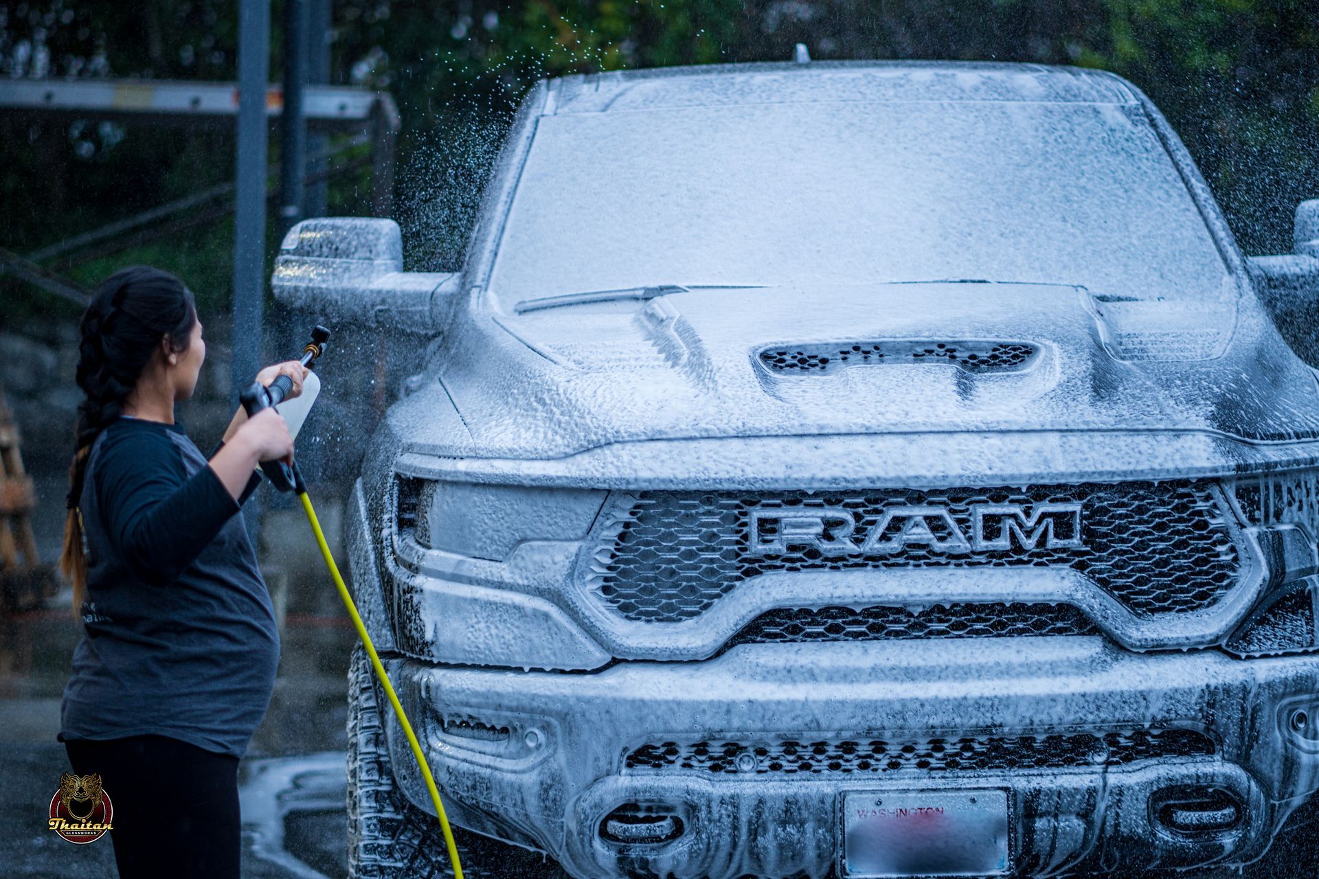 A woman is washing a ram truck with a hose.
