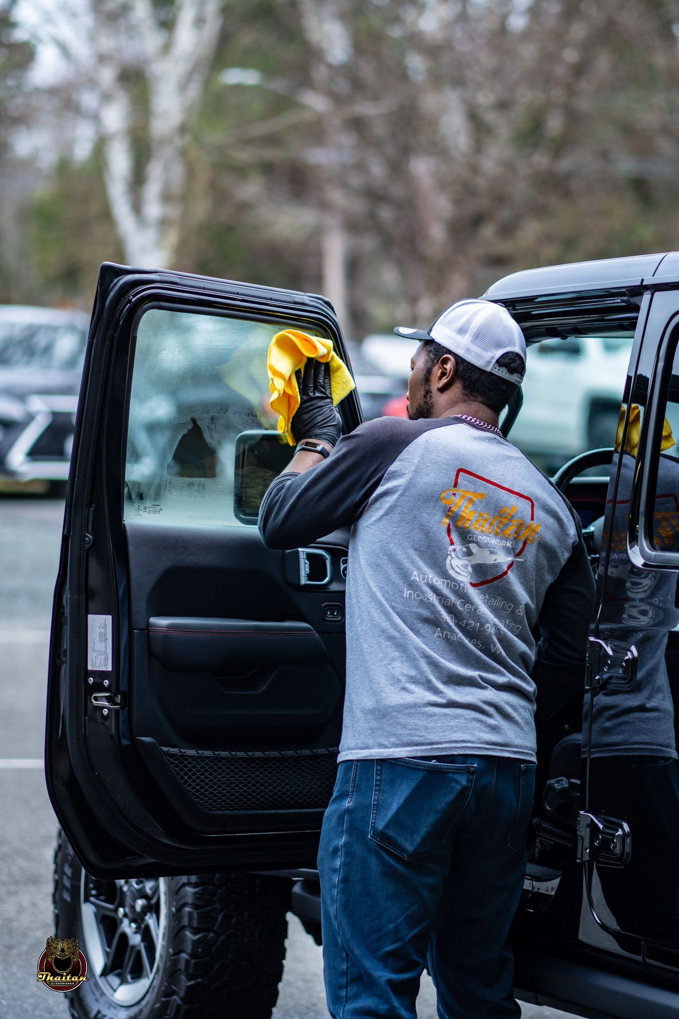 A man is cleaning the windshield of a jeep with a cloth.