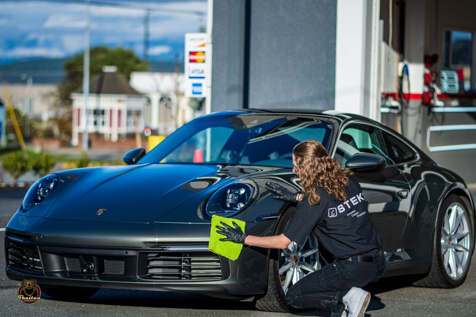 A woman is cleaning a black sports car with a cloth.