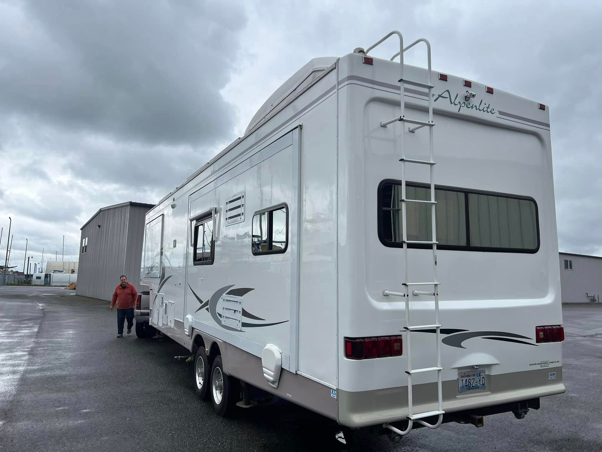 A white rv with a ladder on the back is parked in a parking lot