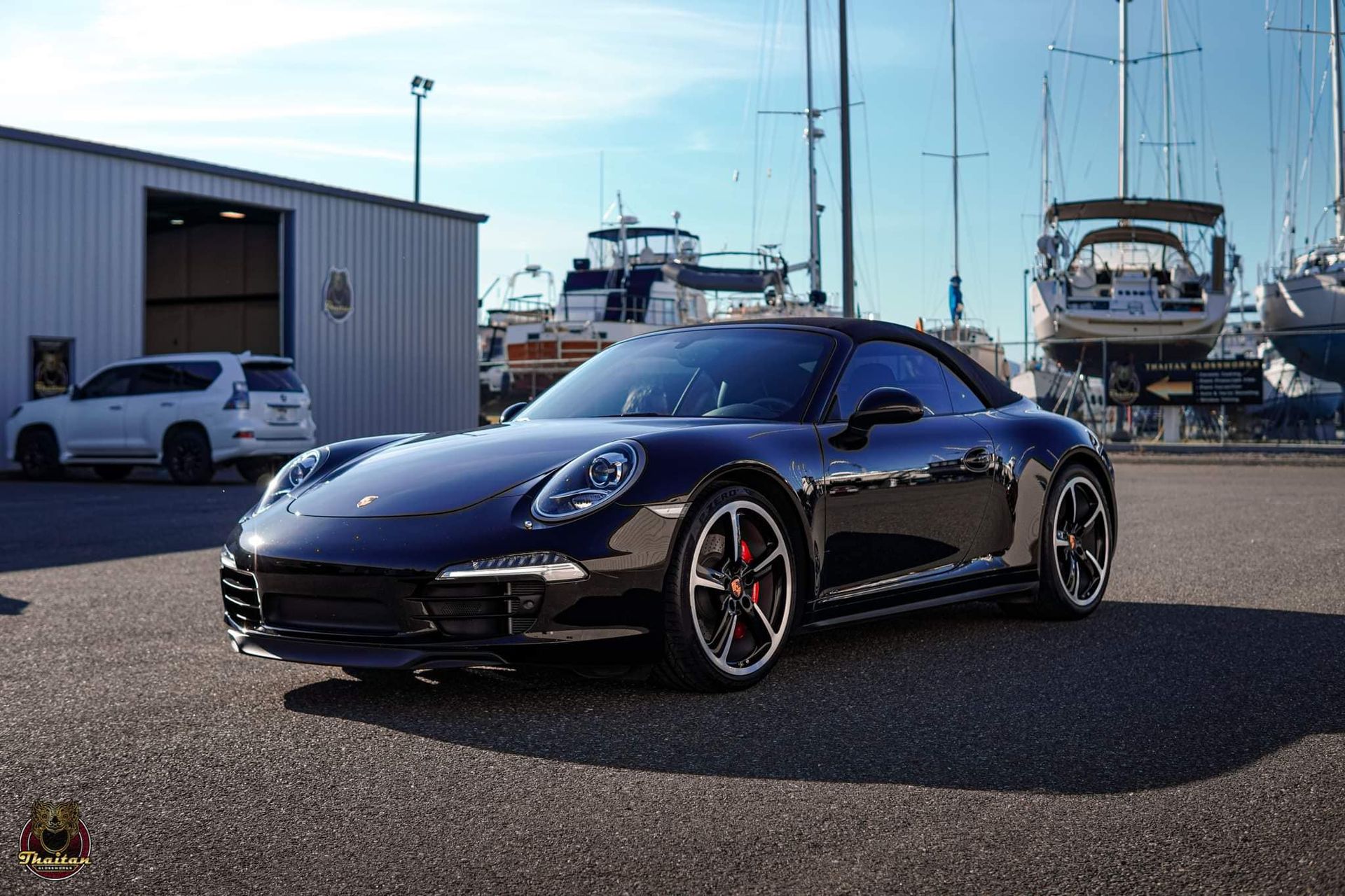 A black porsche 911 cabriolet is parked in front of a boat dock.