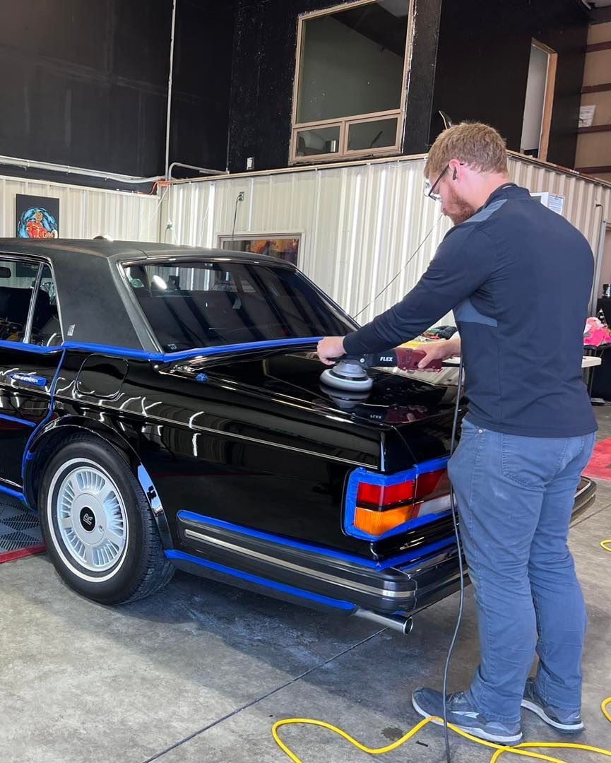 A man is polishing a black car in a garage