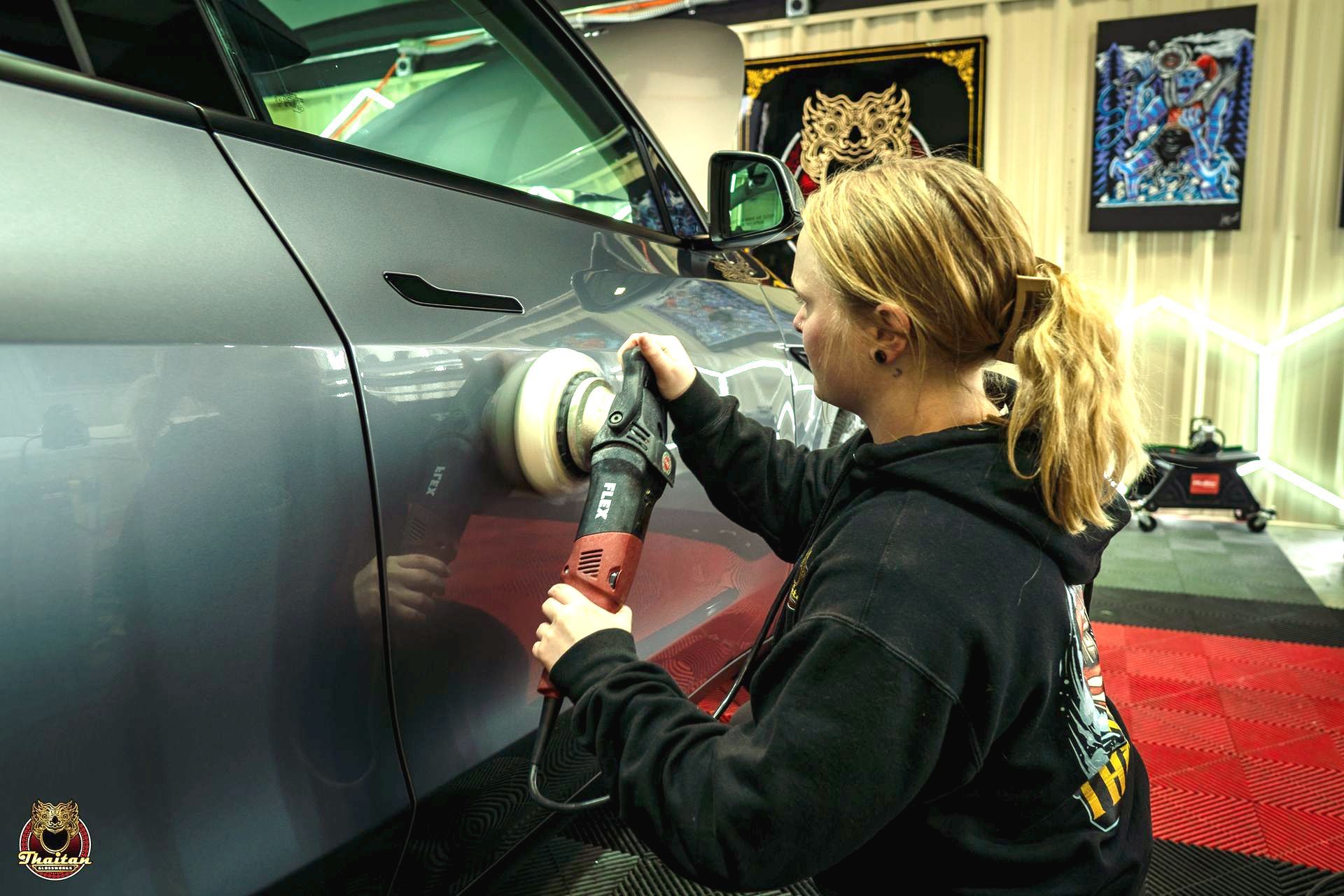 A woman is polishing a car with a machine in a garage.