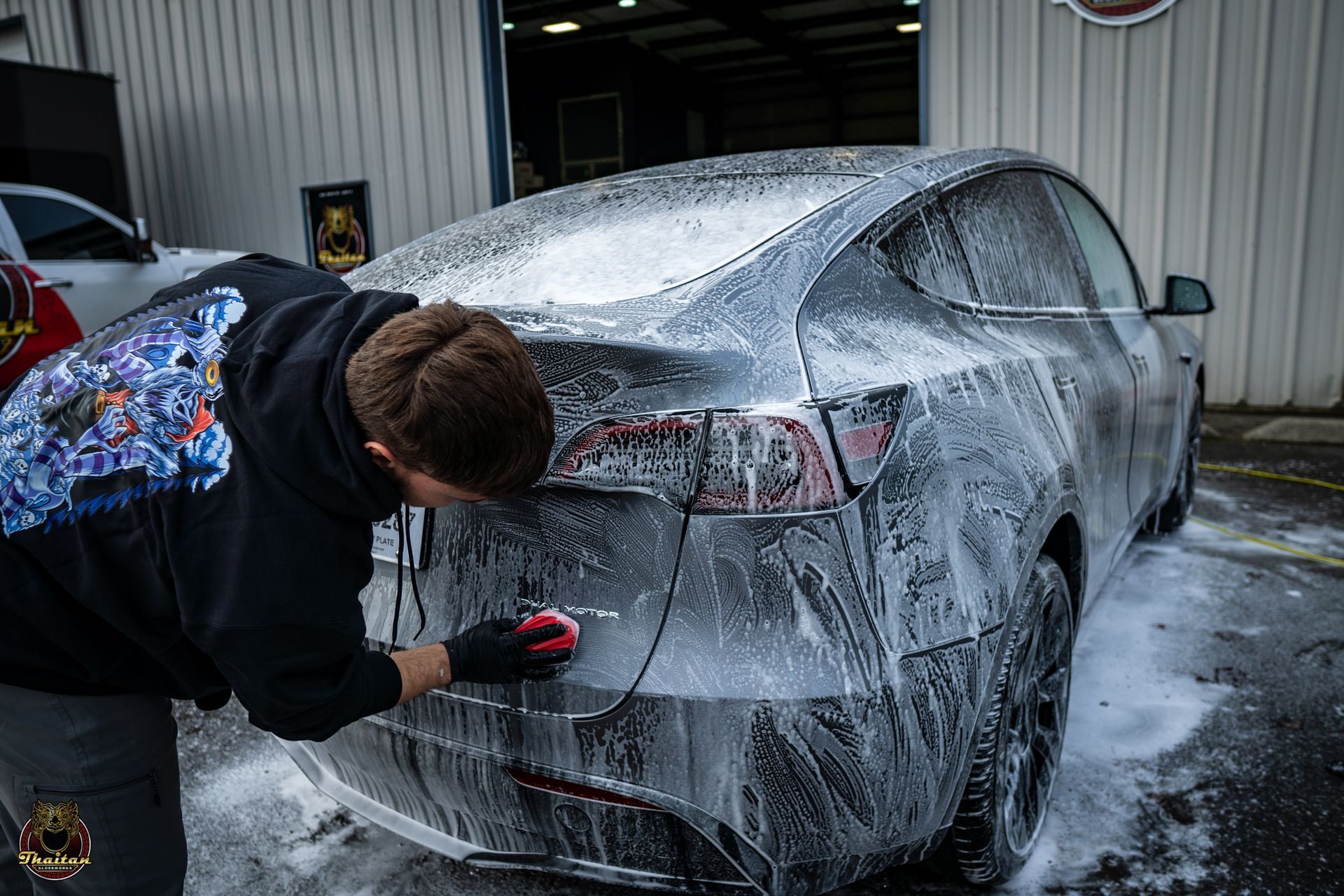 A man is washing a tesla model 3 with foam.