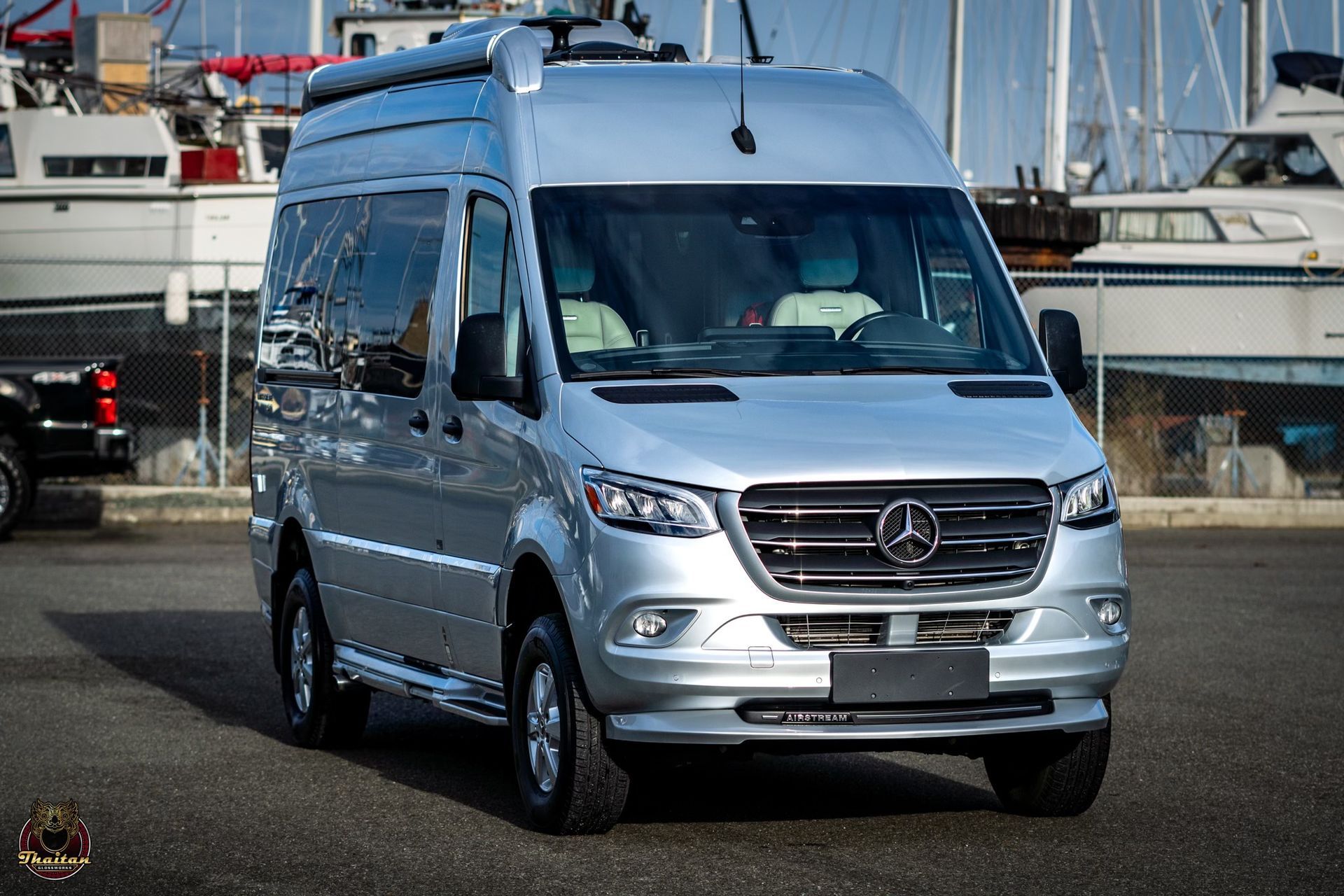 A silver mercedes benz sprinter van is parked in a parking lot.