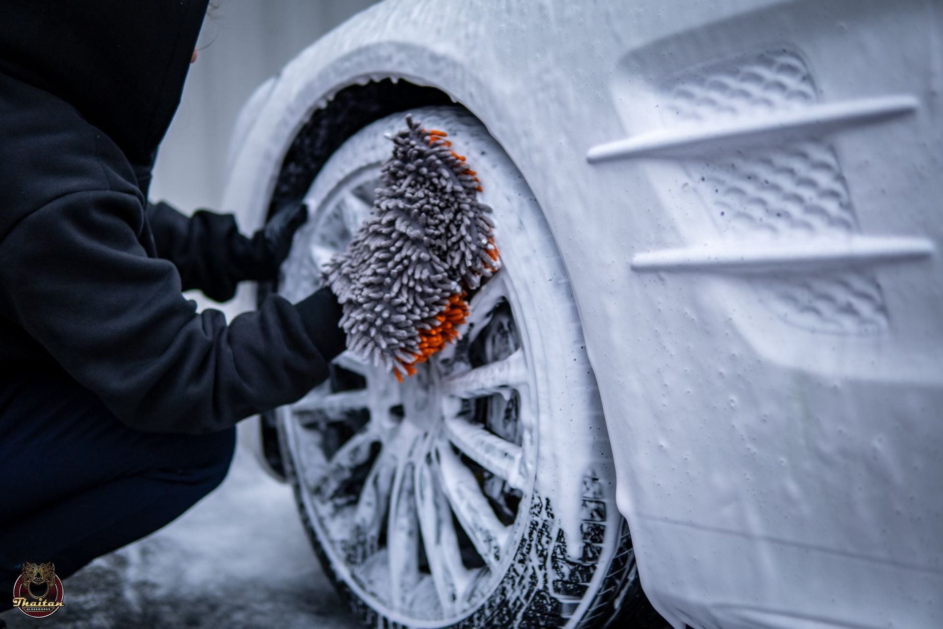 A person is washing a car wheel with a brush.