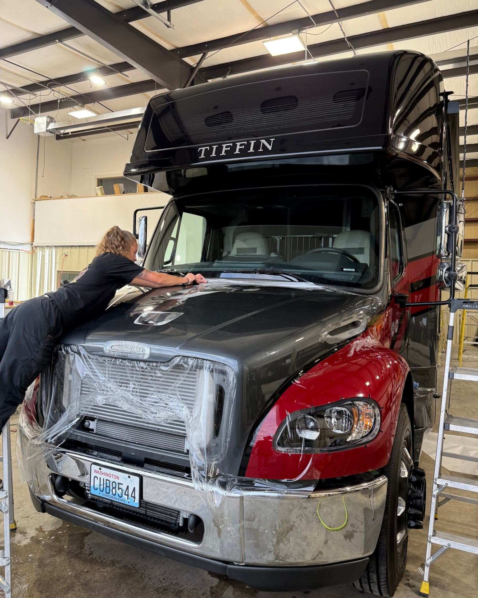 Person washing the hood of a black and red semi truck in a garage