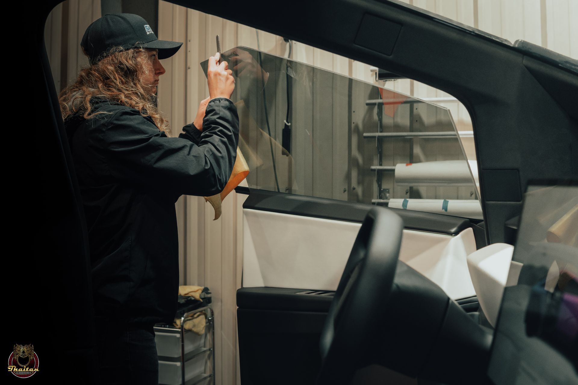 A man with a tattoo on his arm is applying tinted glass to a car window.