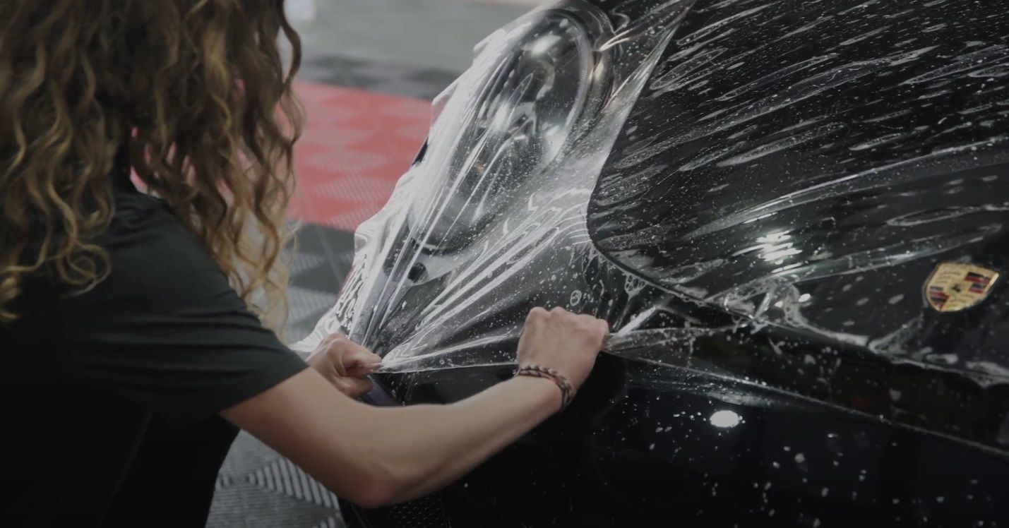 A woman is wrapping a black car with plastic wrap.