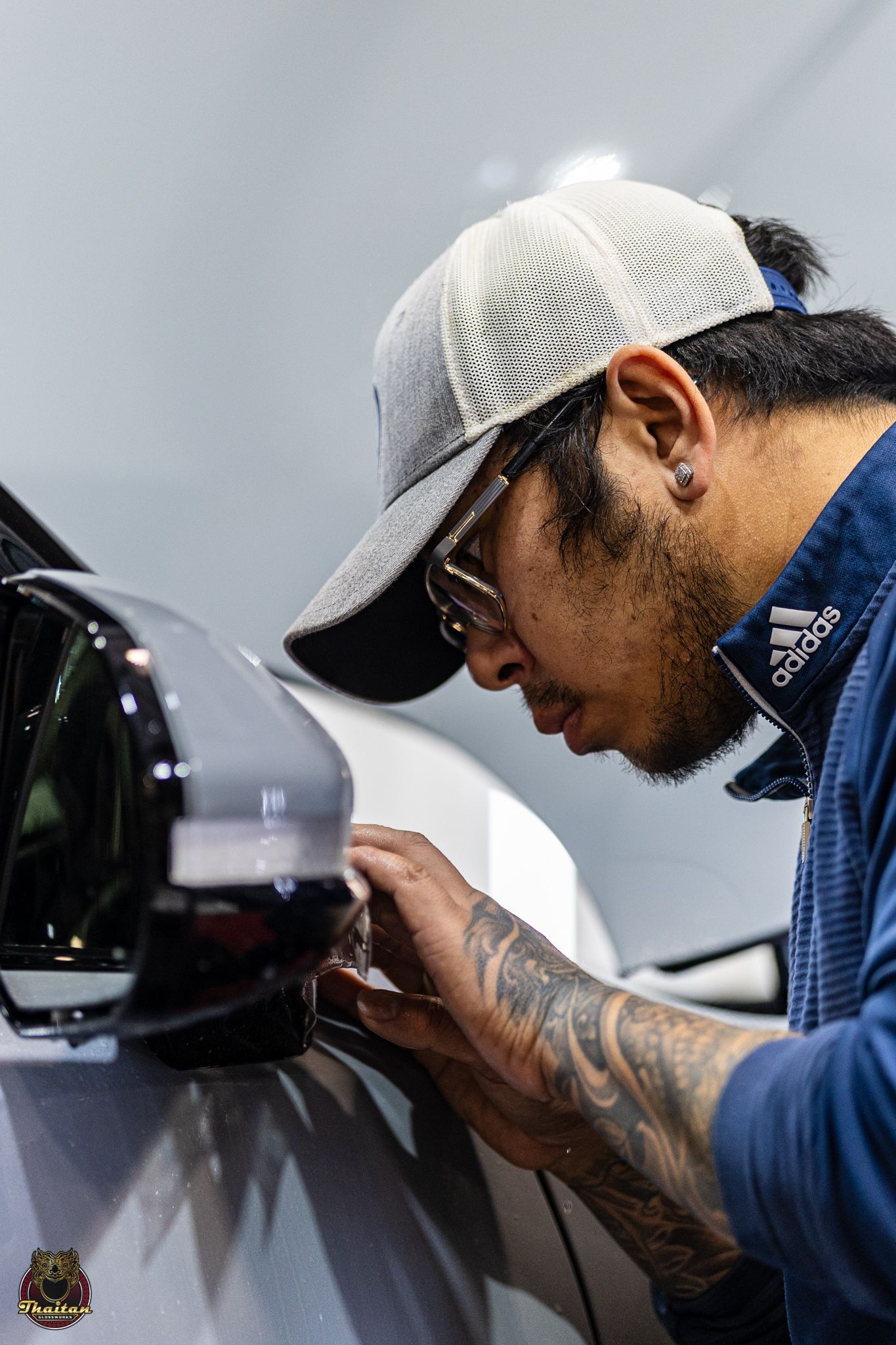 A man wearing a hat and glasses is working on a car.