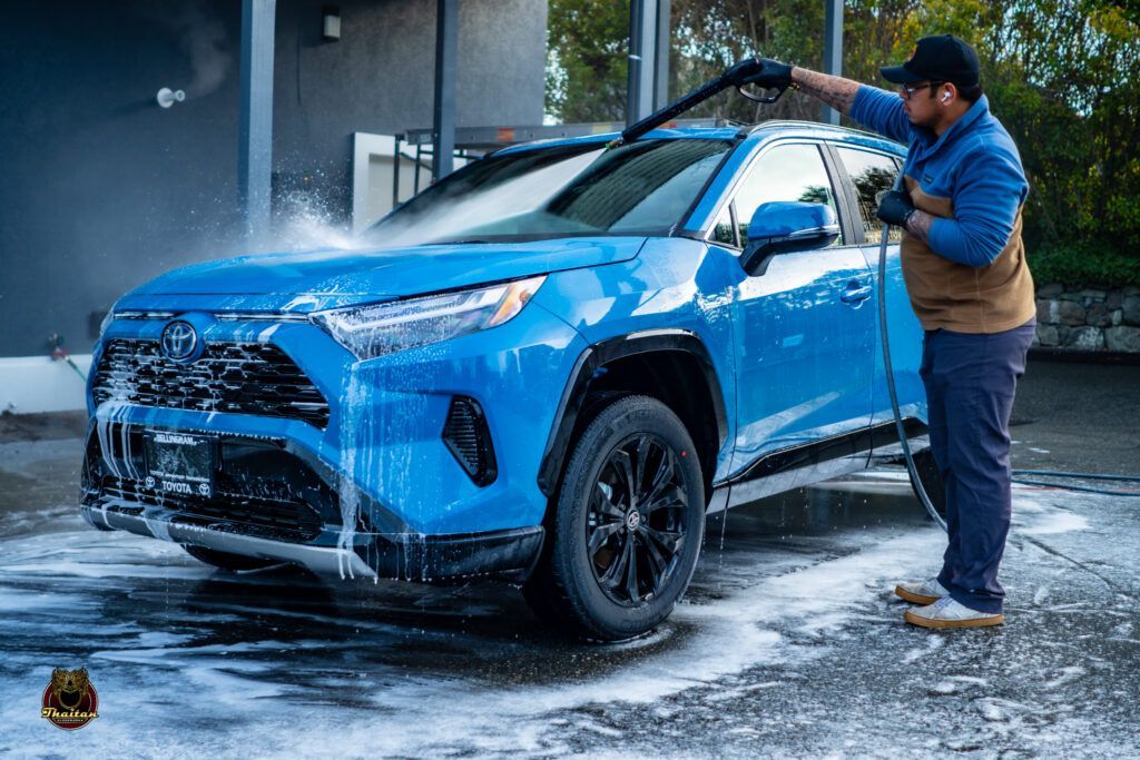 A man is washing a blue car with a high pressure washer.