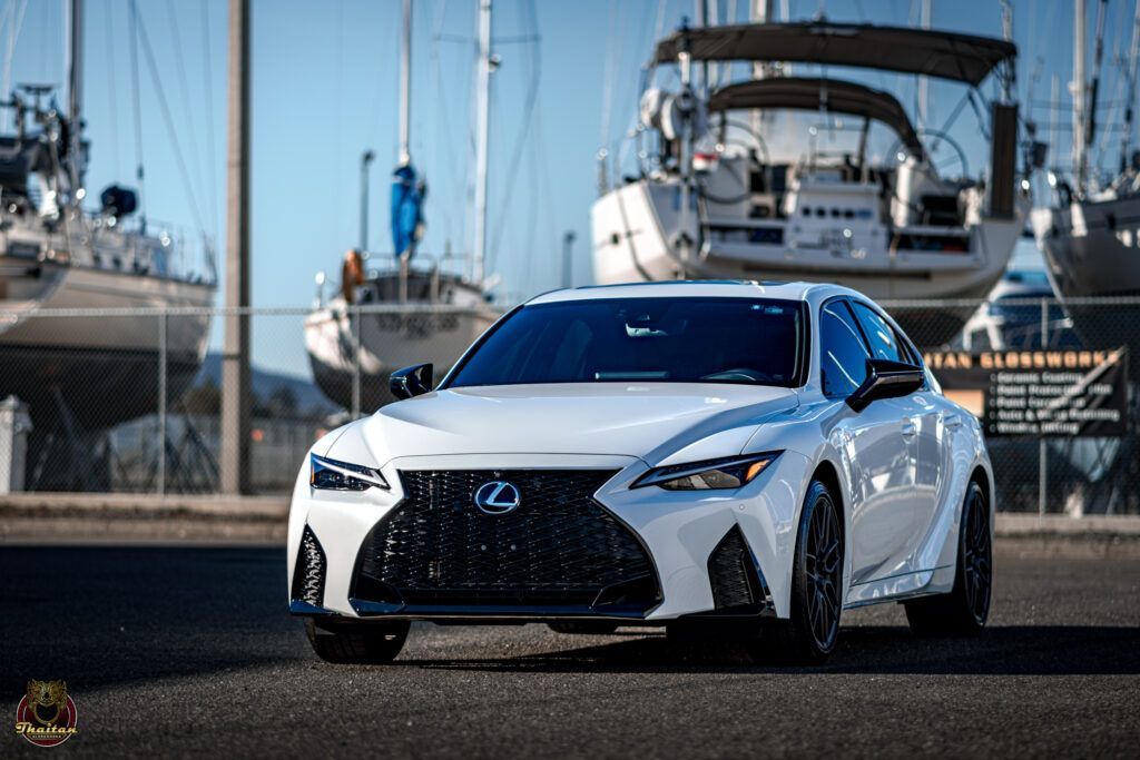 A white lexus is parked in front of boats in a marina.