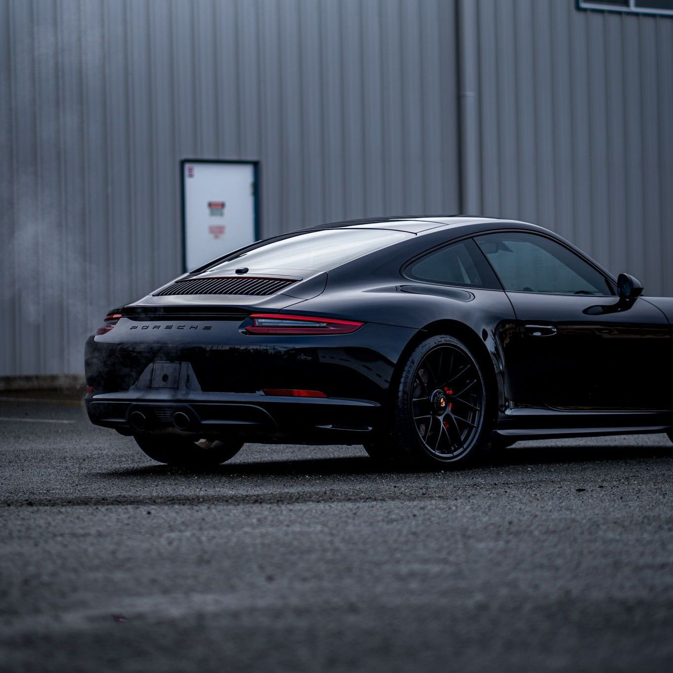 A black porsche 911 is parked in front of a building.