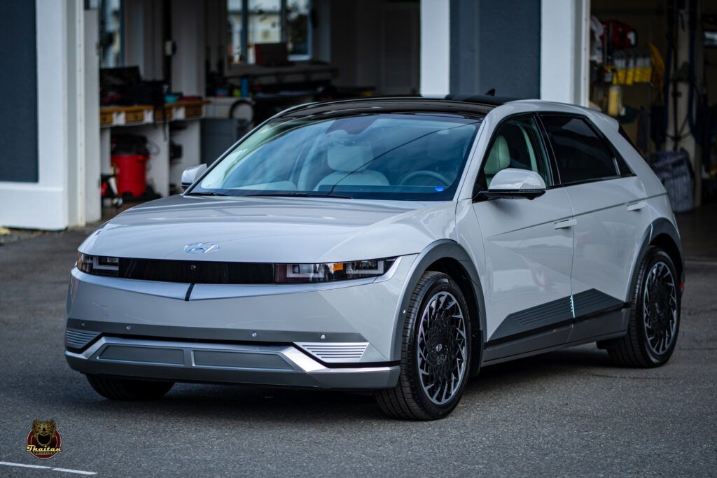 A silver electric car is parked in front of a garage.