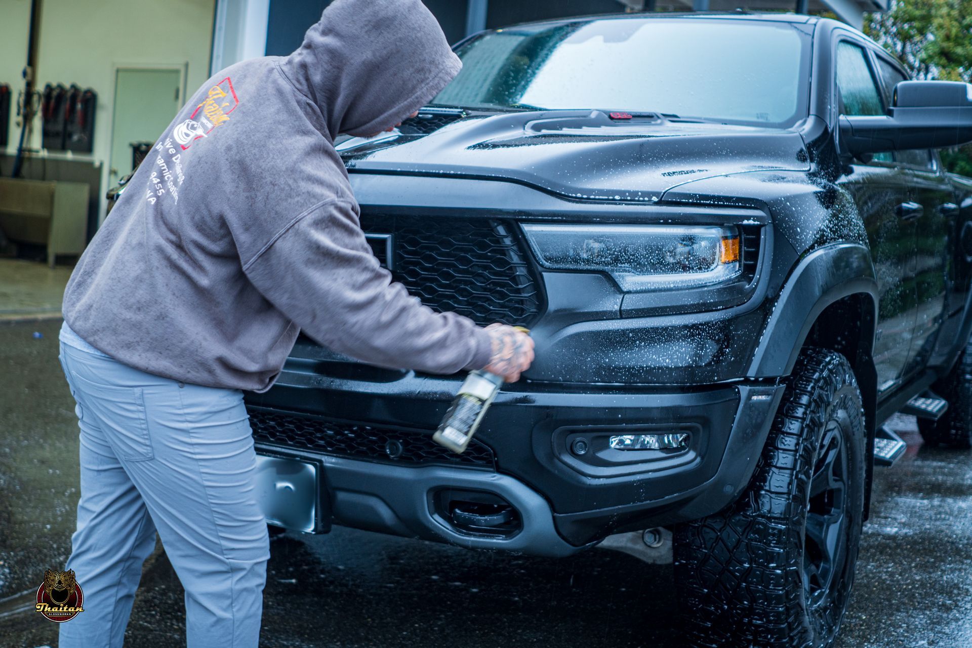 A man in a hoodie is washing a black truck.