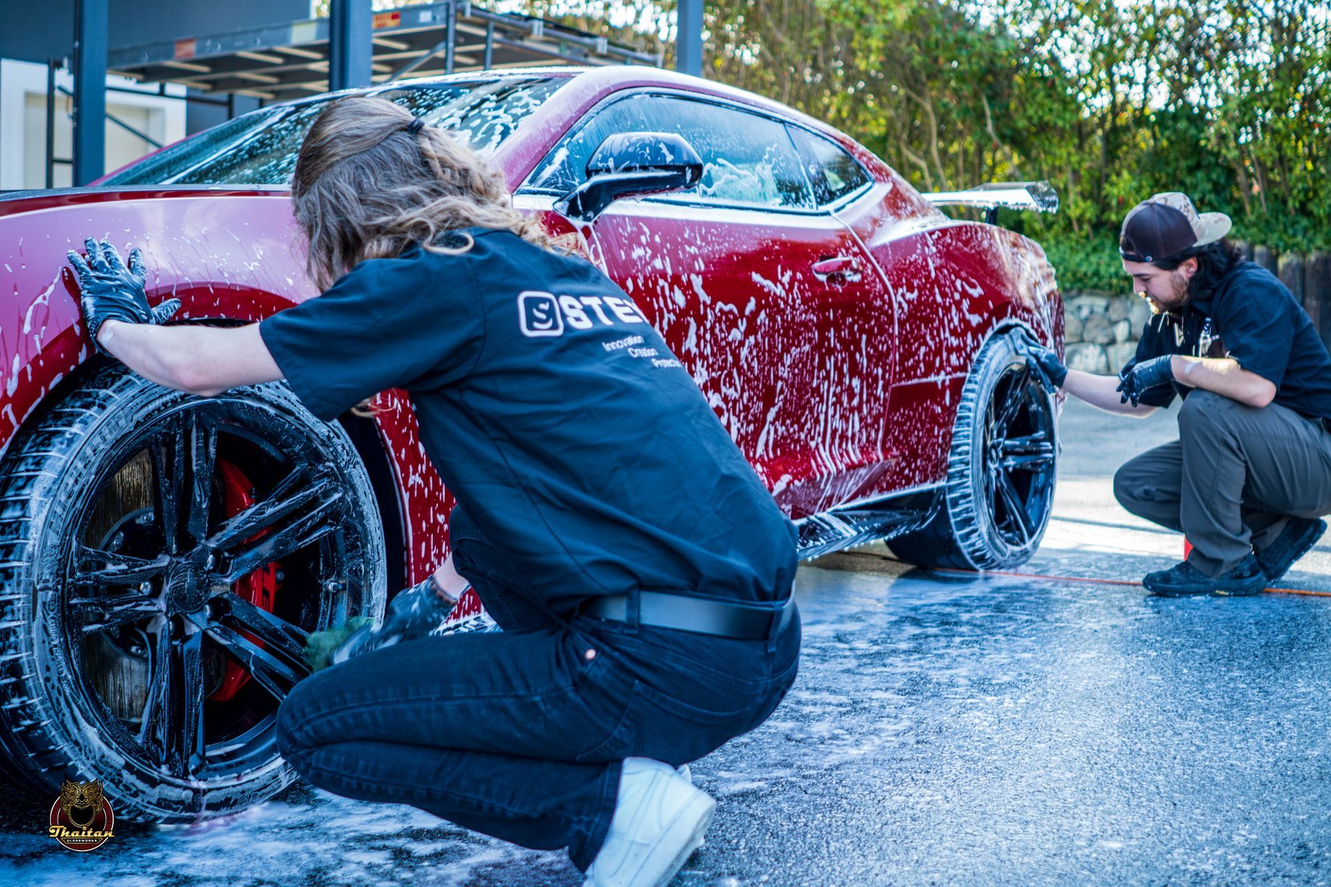 Two men are kneeling down to wash a red sports car.