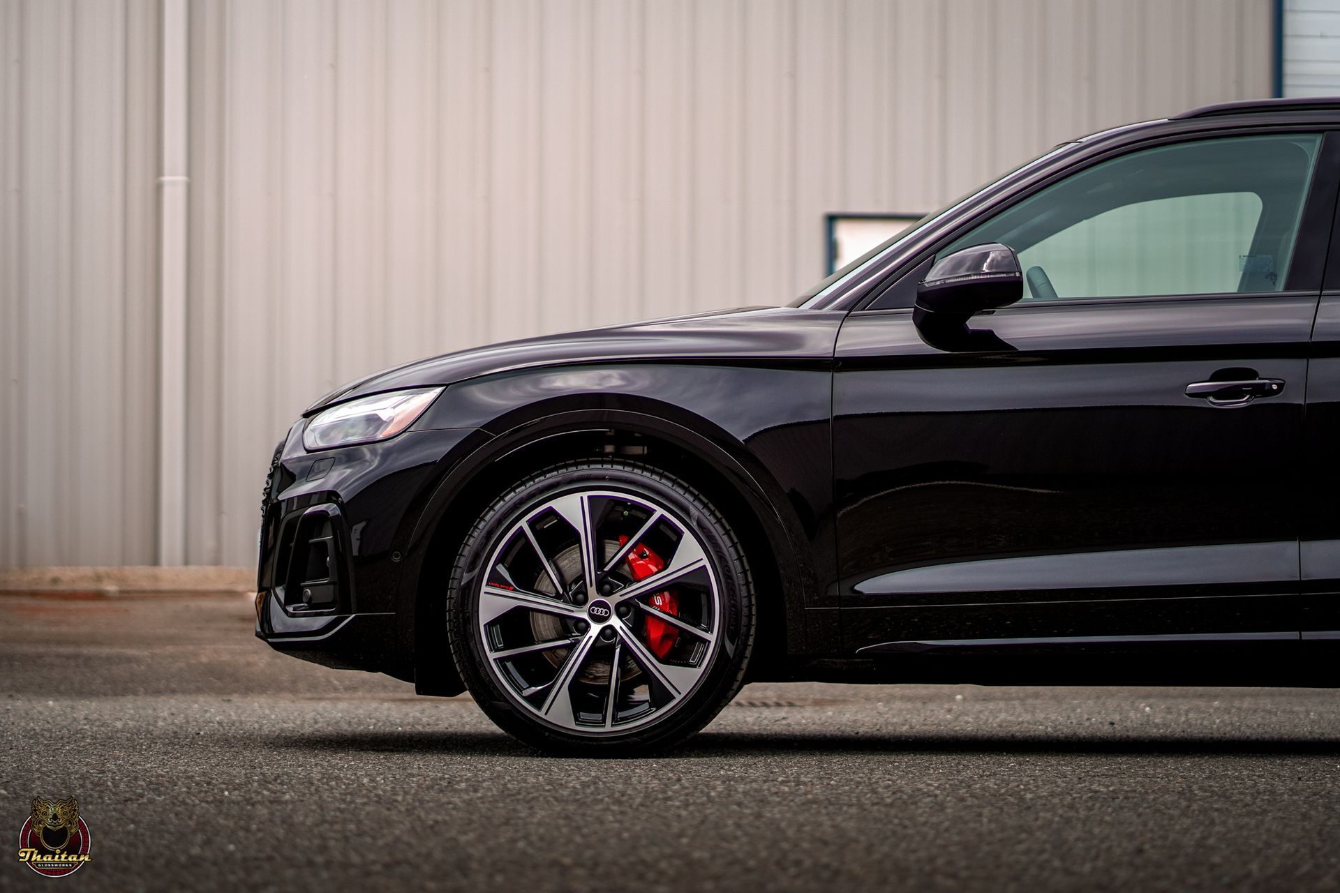 A black car with red brake calipers is parked in front of a building.