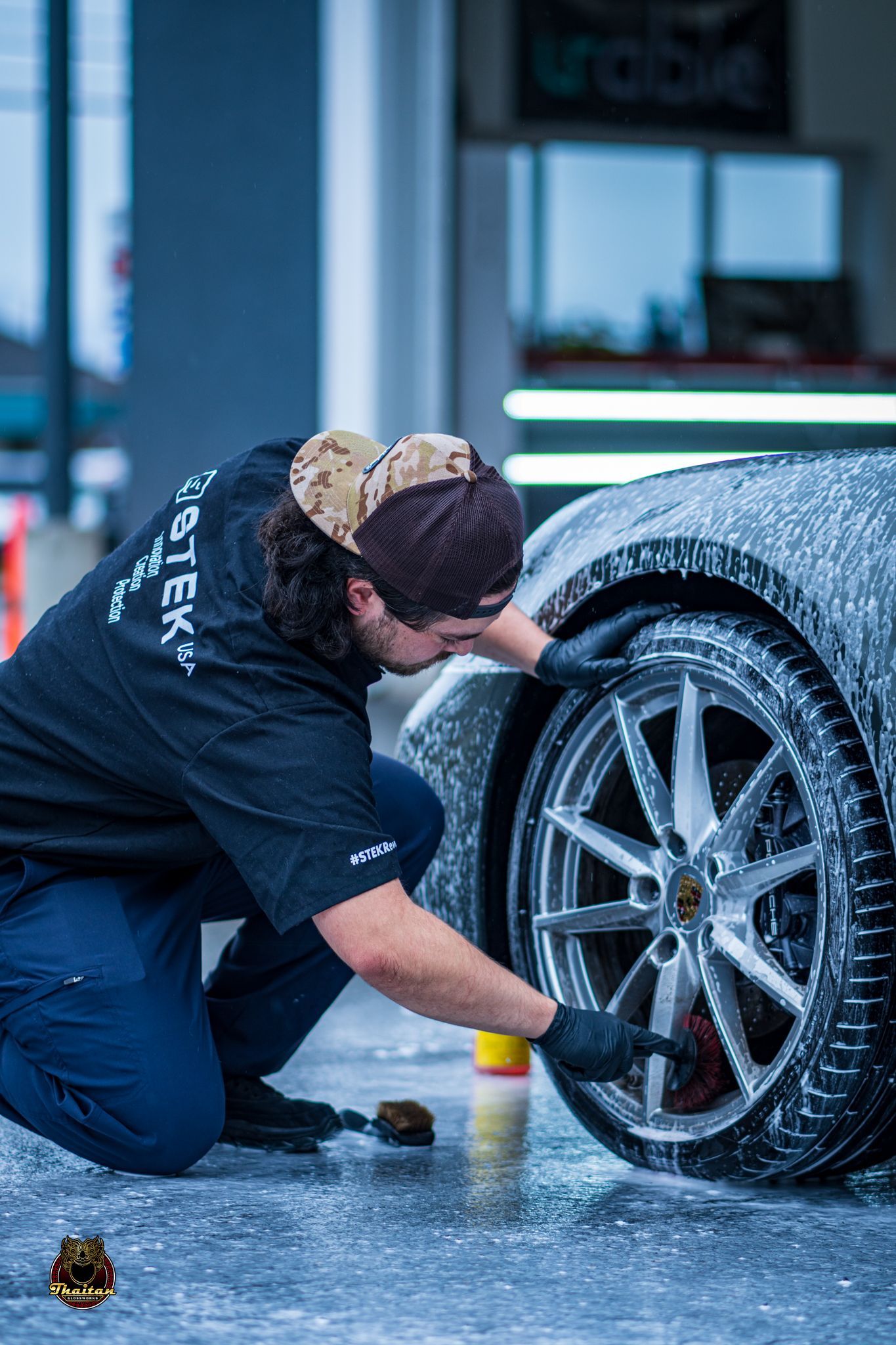 A man is kneeling down to wash a car wheel.