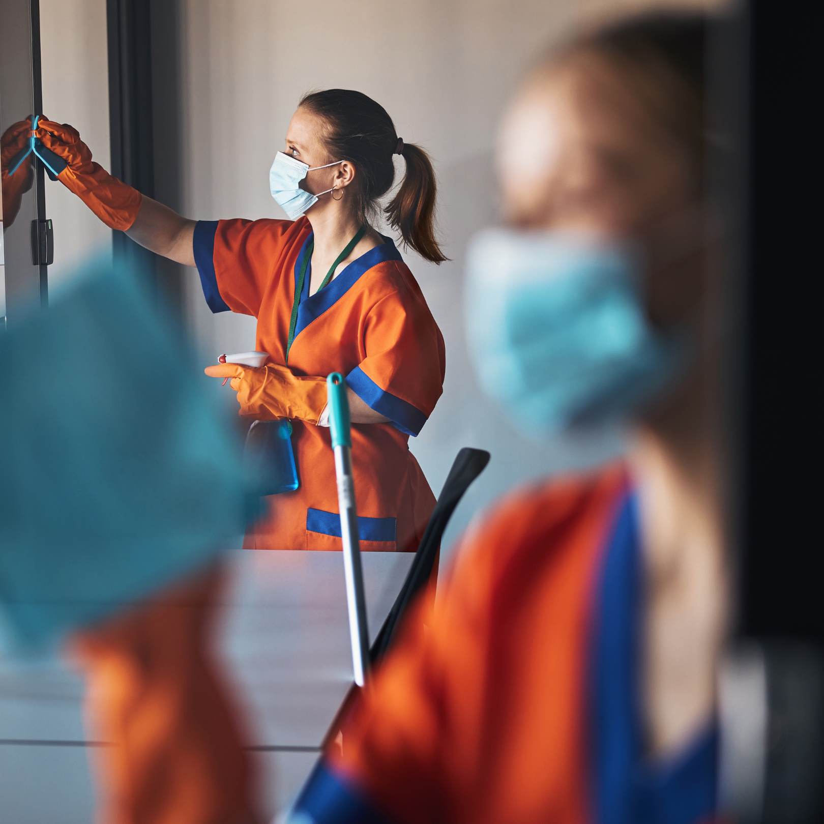 A woman wearing a mask and gloves is cleaning a window.