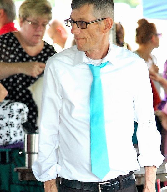 Man in white shirt, light blue tie, black pants, glasses, outdoors, looking right.