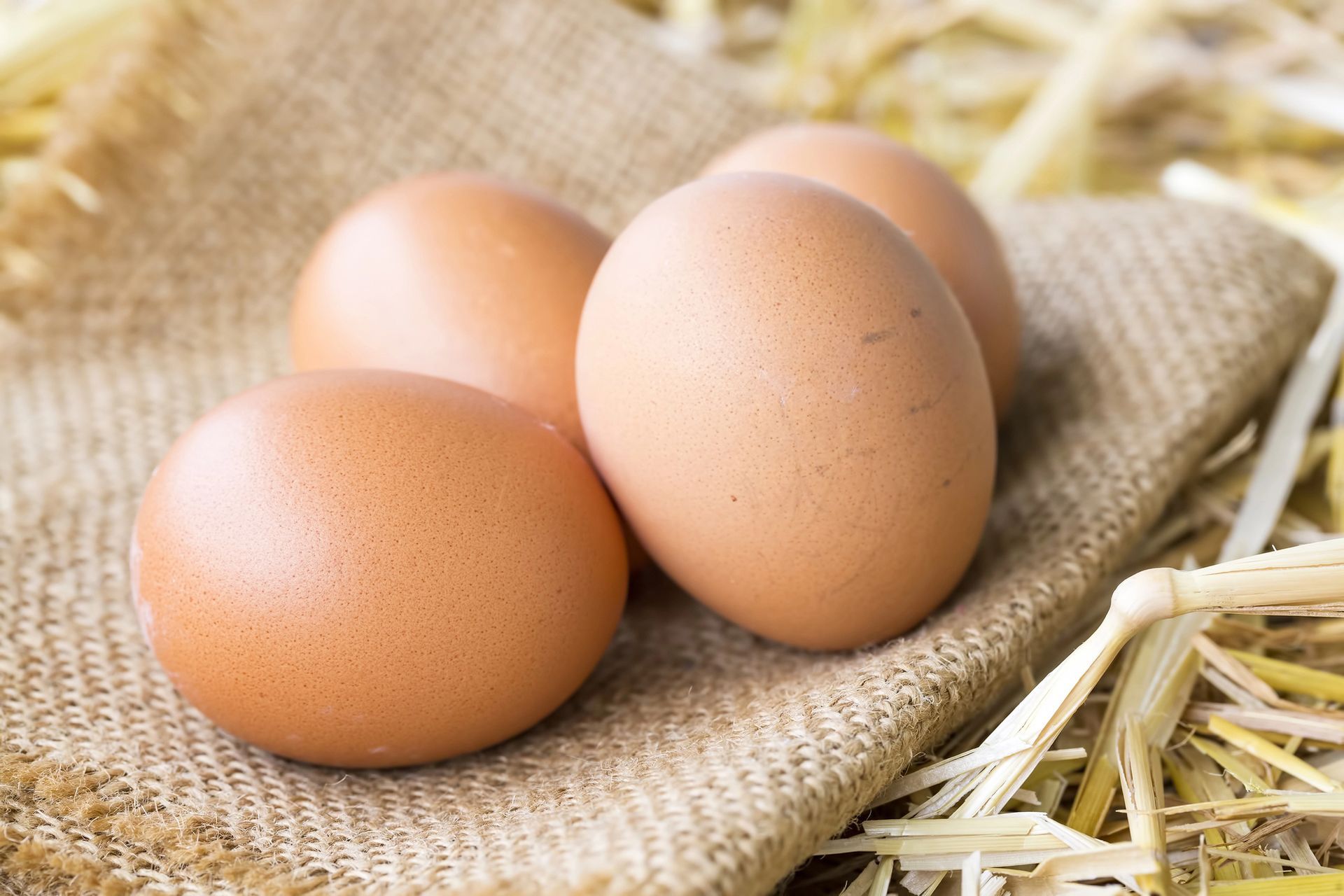Quattro uova marroni su una tela di iuta, appoggiate sulla paglia.