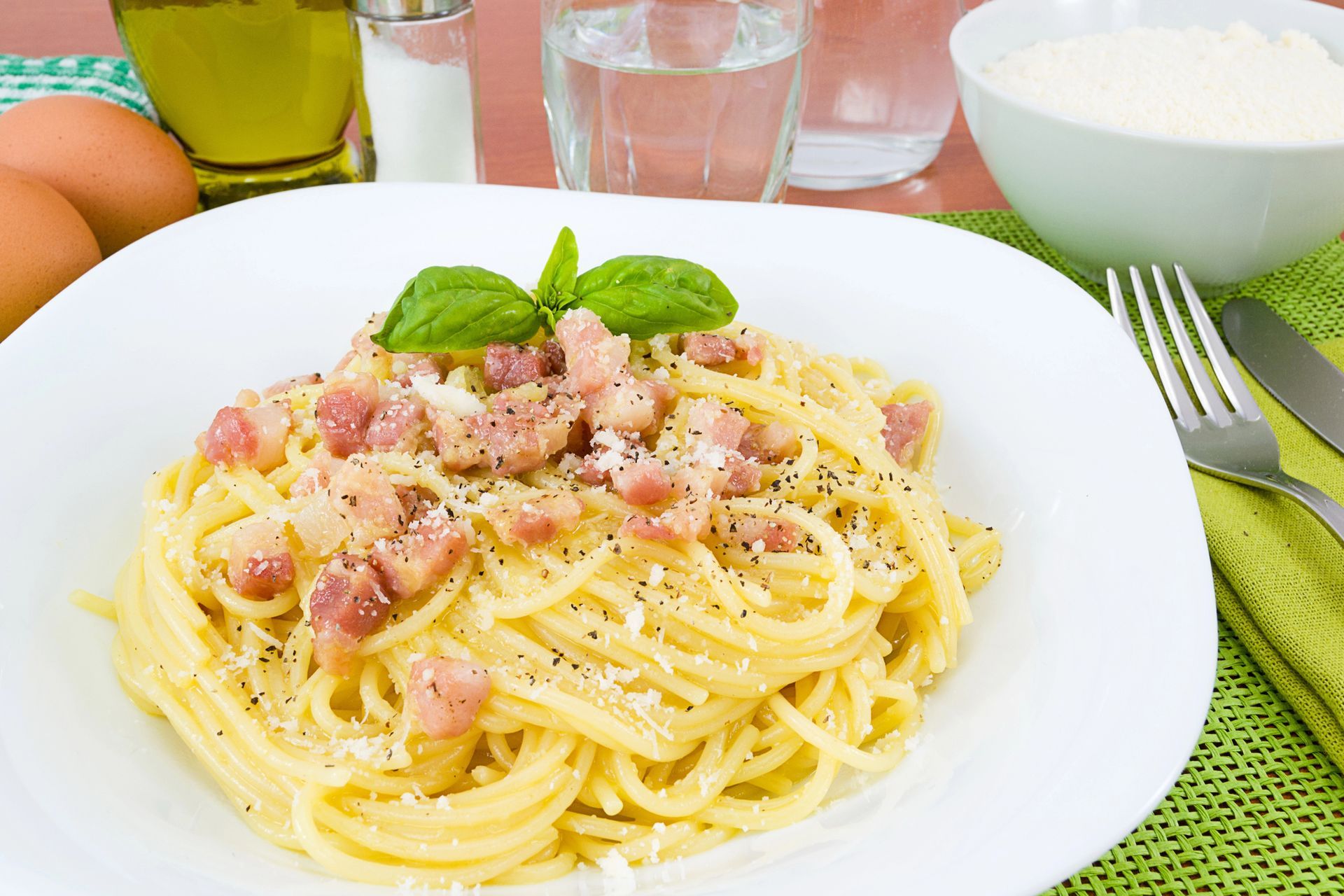 Spaghetti alla carbonara con pancetta, guarniti con basilico, serviti su un piatto bianco.