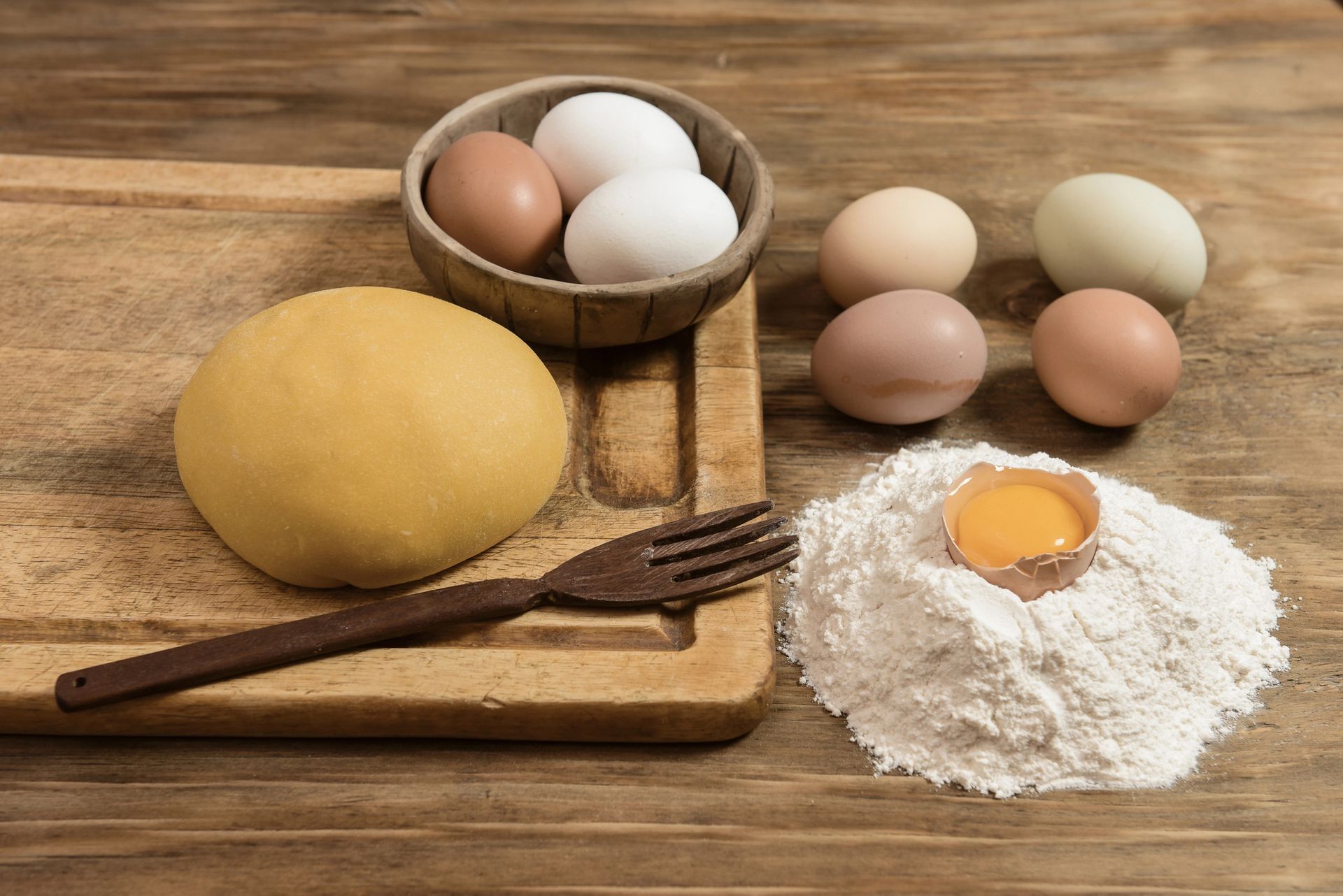 Palla di pasta, uova, farina e una forchetta su una tavola di legno: ingredienti per la cottura.