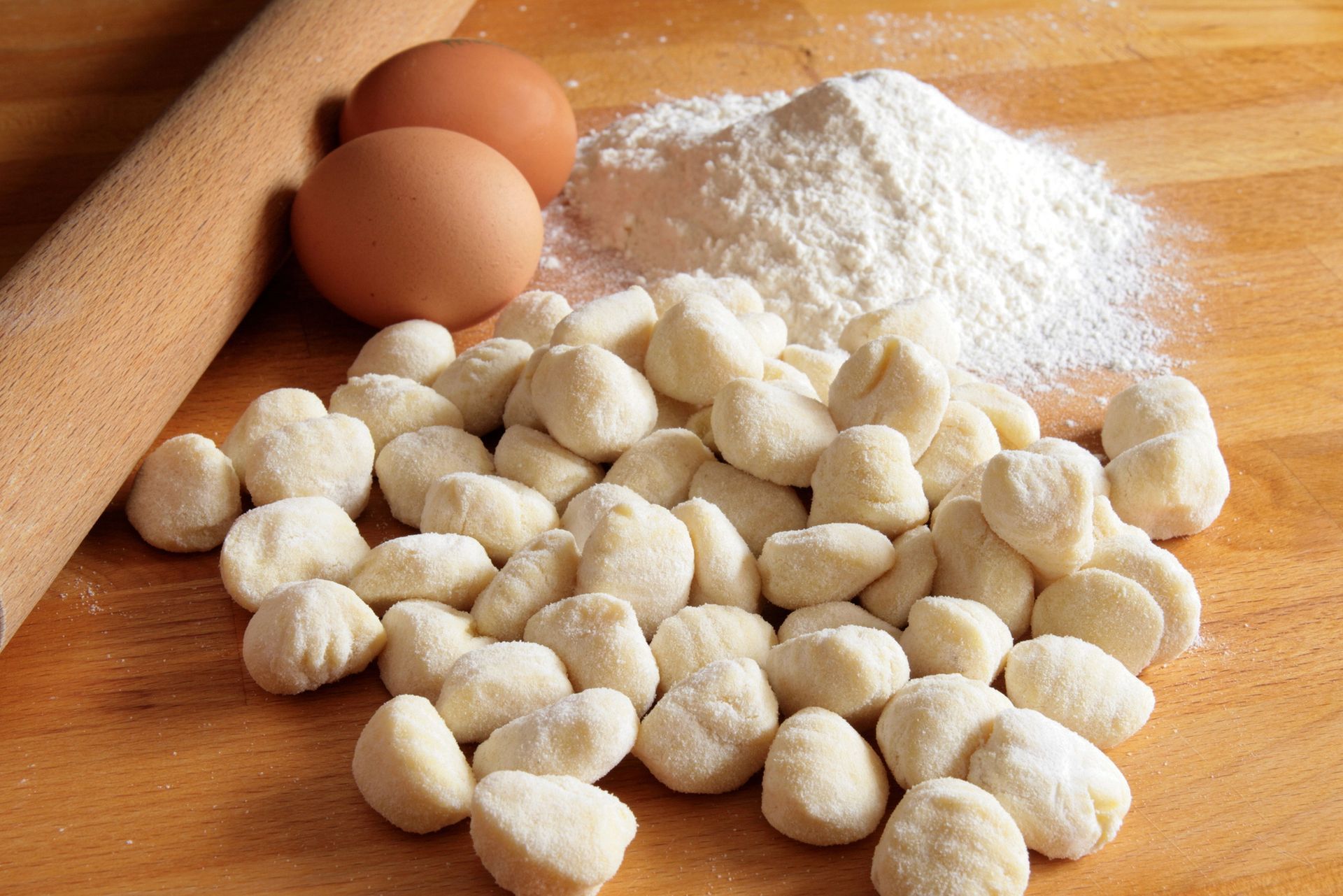 Gnocchi con ingredienti: uova, farina e mattarello su una superficie di legno.