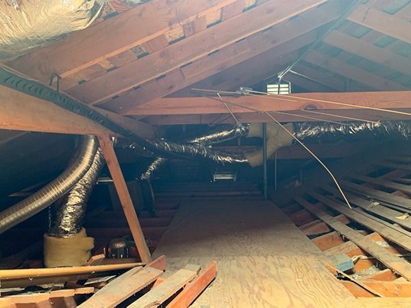 An attic with a lot of pipes and wires hanging from the ceiling.