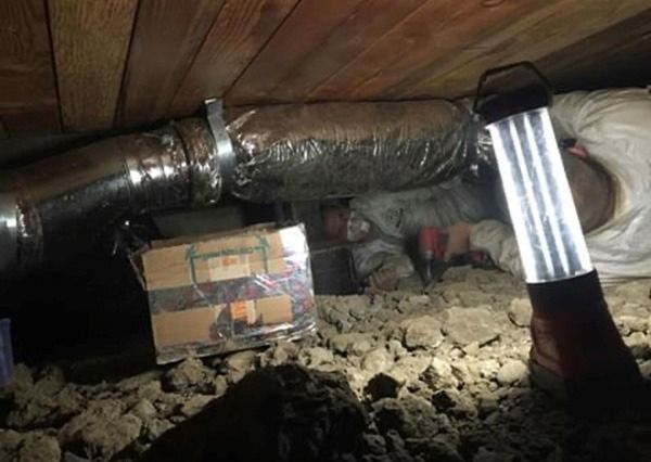 A person is laying under a ceiling in a basement with a lantern.