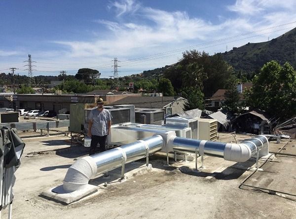 A man is standing on top of a roof next to a large pipe.