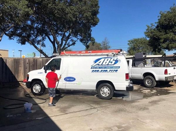 A man is washing a white van with ABS Heating and Air Conditioning written on it