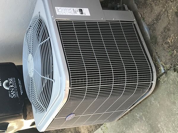 A Carrier air conditioning is sitting on the ground next to a trash can.