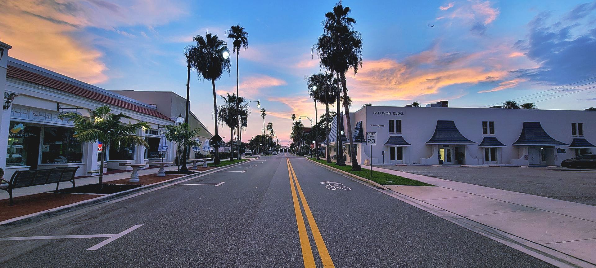 A street with palm trees on the side of it and a sunset in the background.