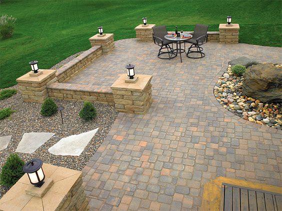 Stone patio with seating, surrounded by landscaping and low walls with lights.