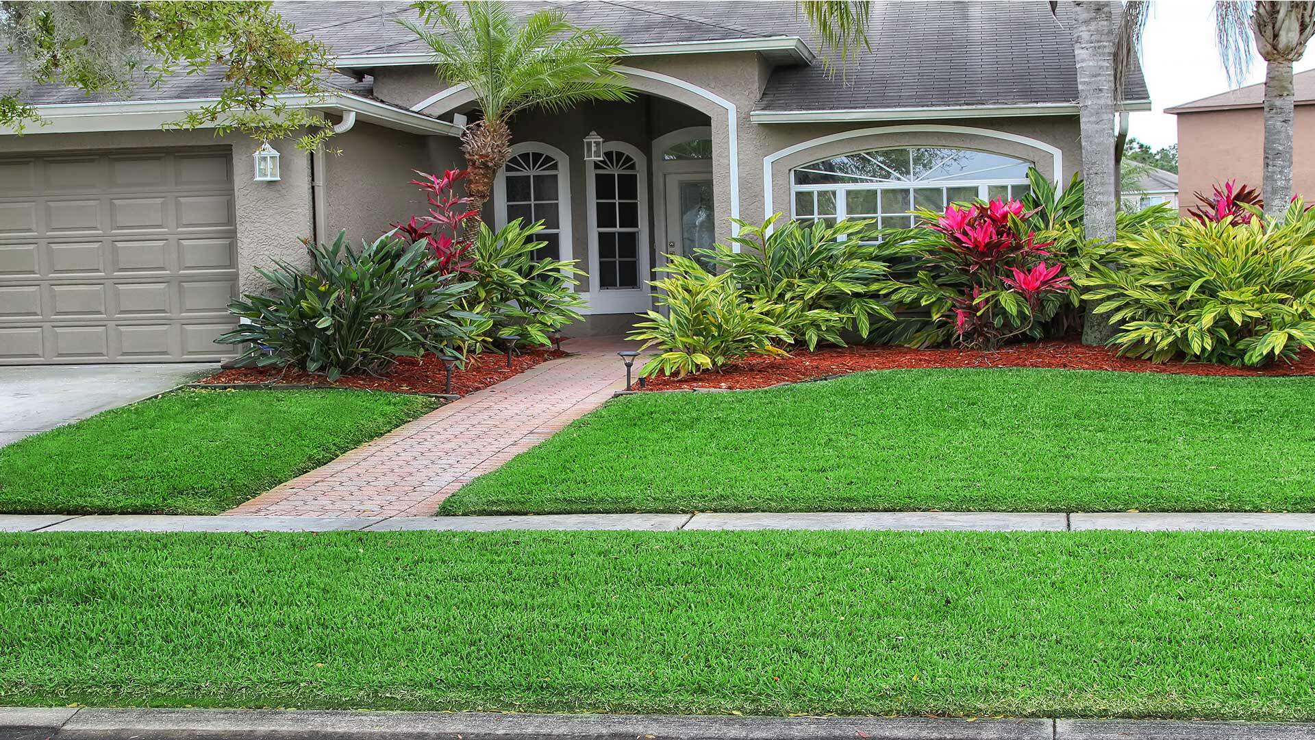 House exterior with green lawn, brick pathway, and colorful landscaping.