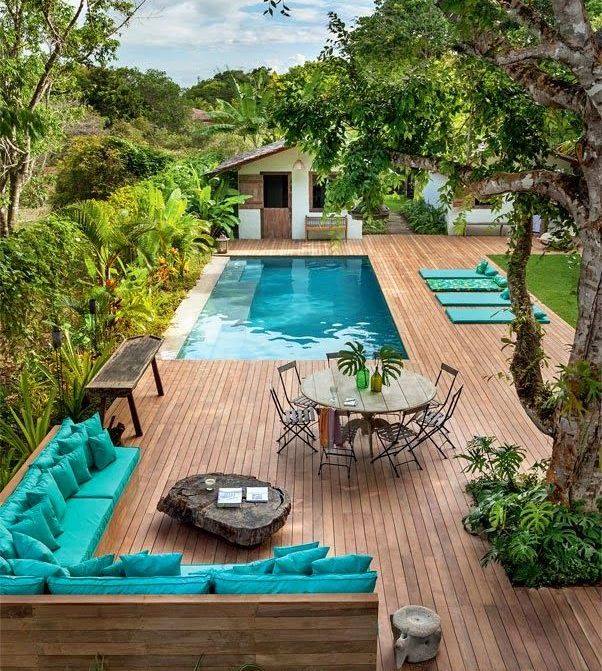 Wooden deck with pool, turquoise seating, dining area, and lush greenery.