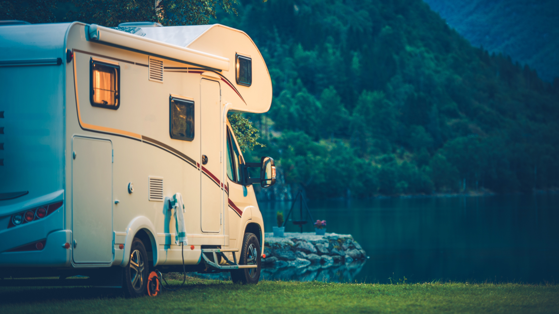 A rv is parked on the grass next to a lake.
