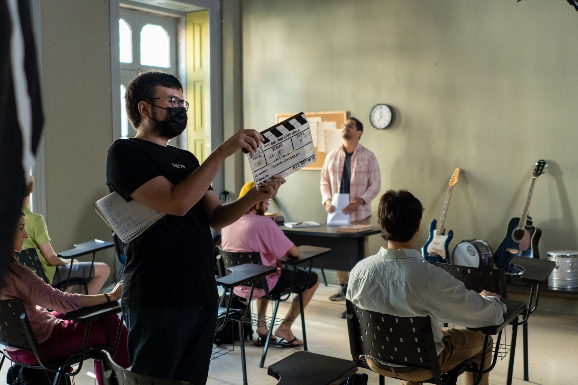 A man is holding a clapper board in front of a group of people in a classroom.